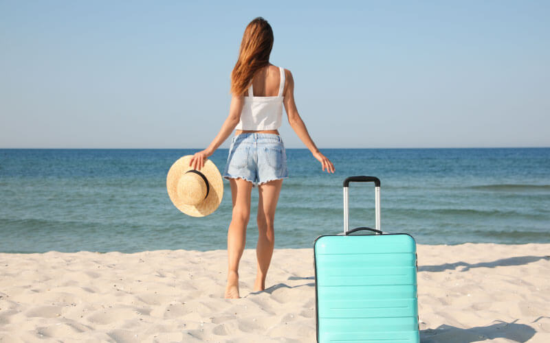 mujer visitando las playas de cancun por primera vez, tiene una maleta azul y un sombrero en la mano